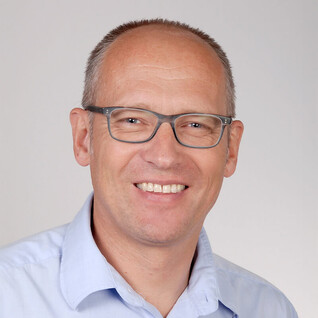 Portrait eines Mannes mit Brille und kurzem Haar, freundlich blickend.